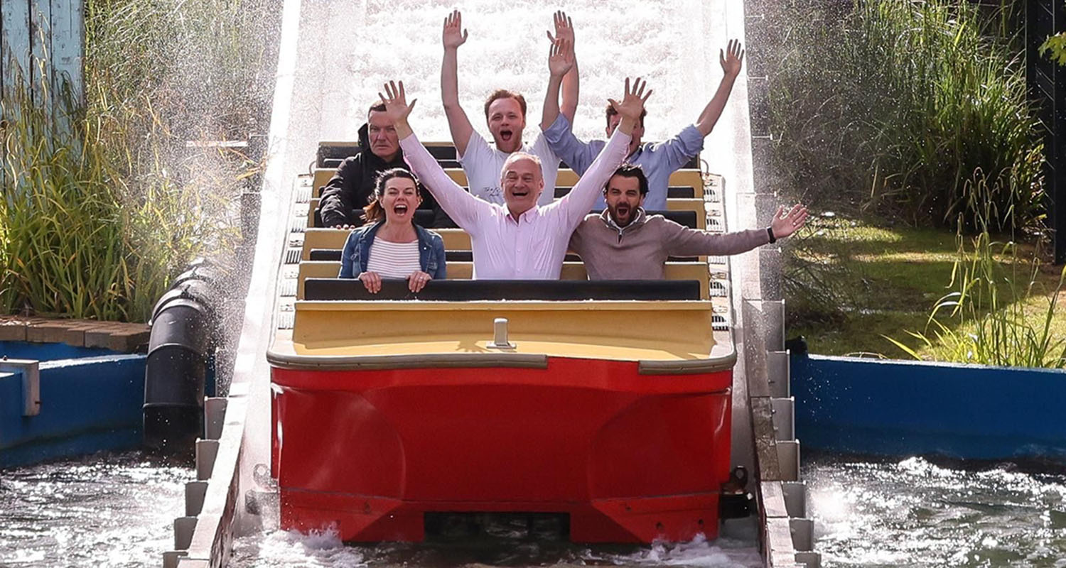 Ed Davey on a water shoot ride with his arms held up.