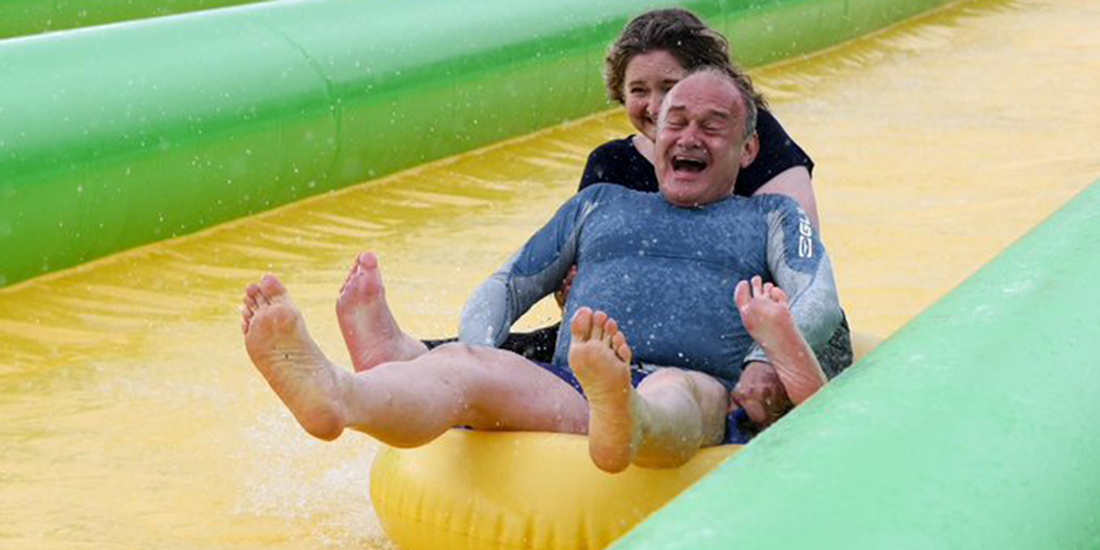 Ed Davey slides down a water slide on a yellow ring.