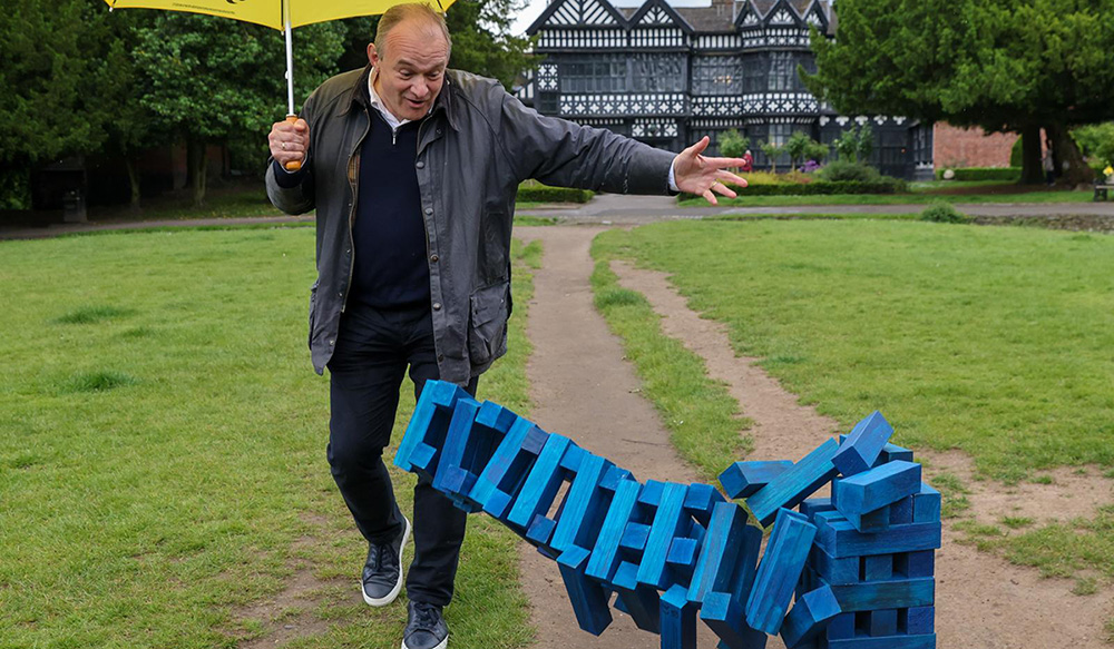 Ed watching as a giant stack of blue-brick jenga falls down.