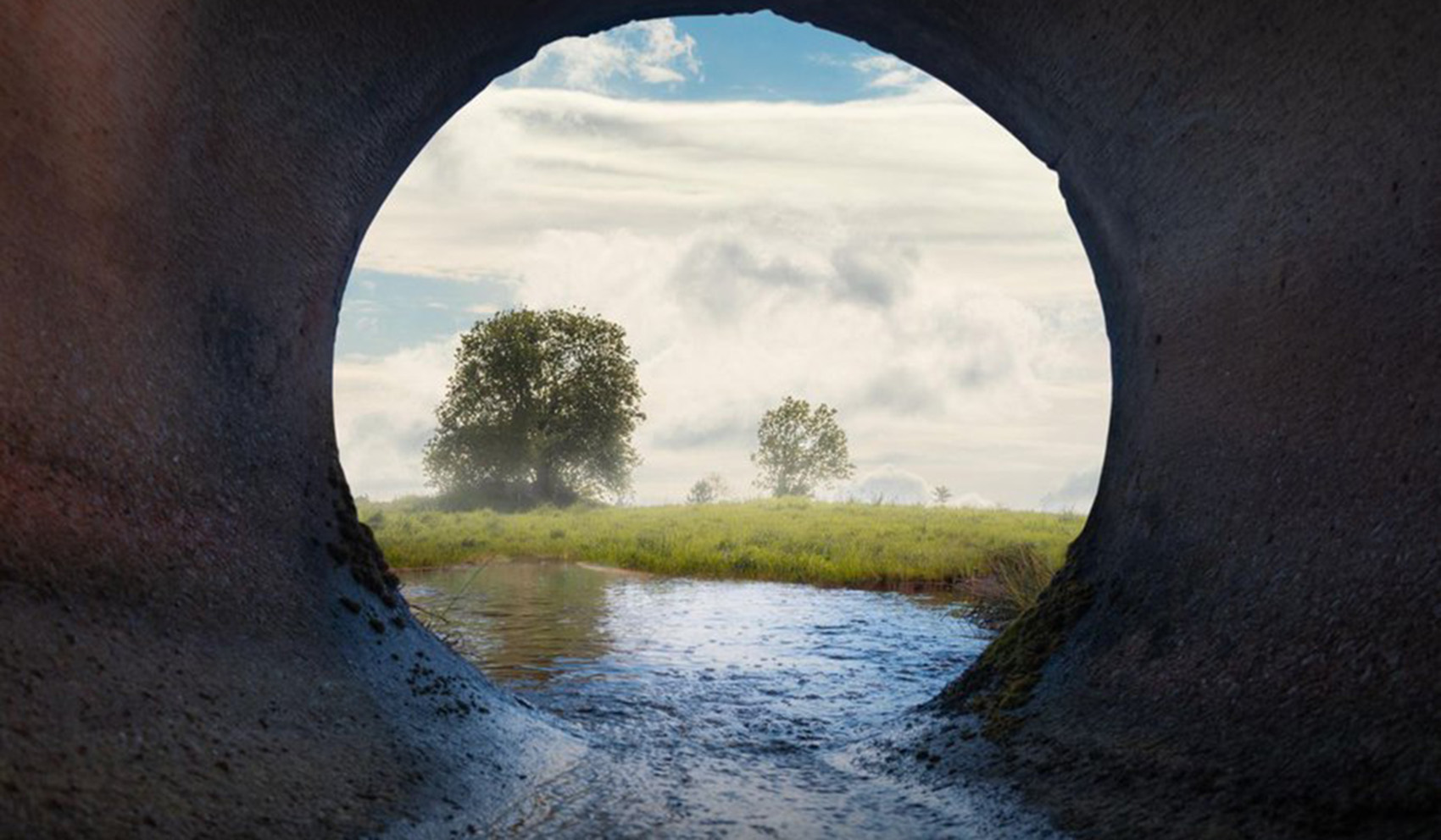 Looking through a pipe with water gushing through it and into a river.