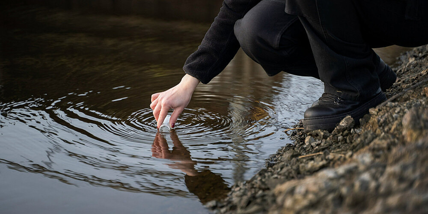 Water sample being taken from a river with a test tube.