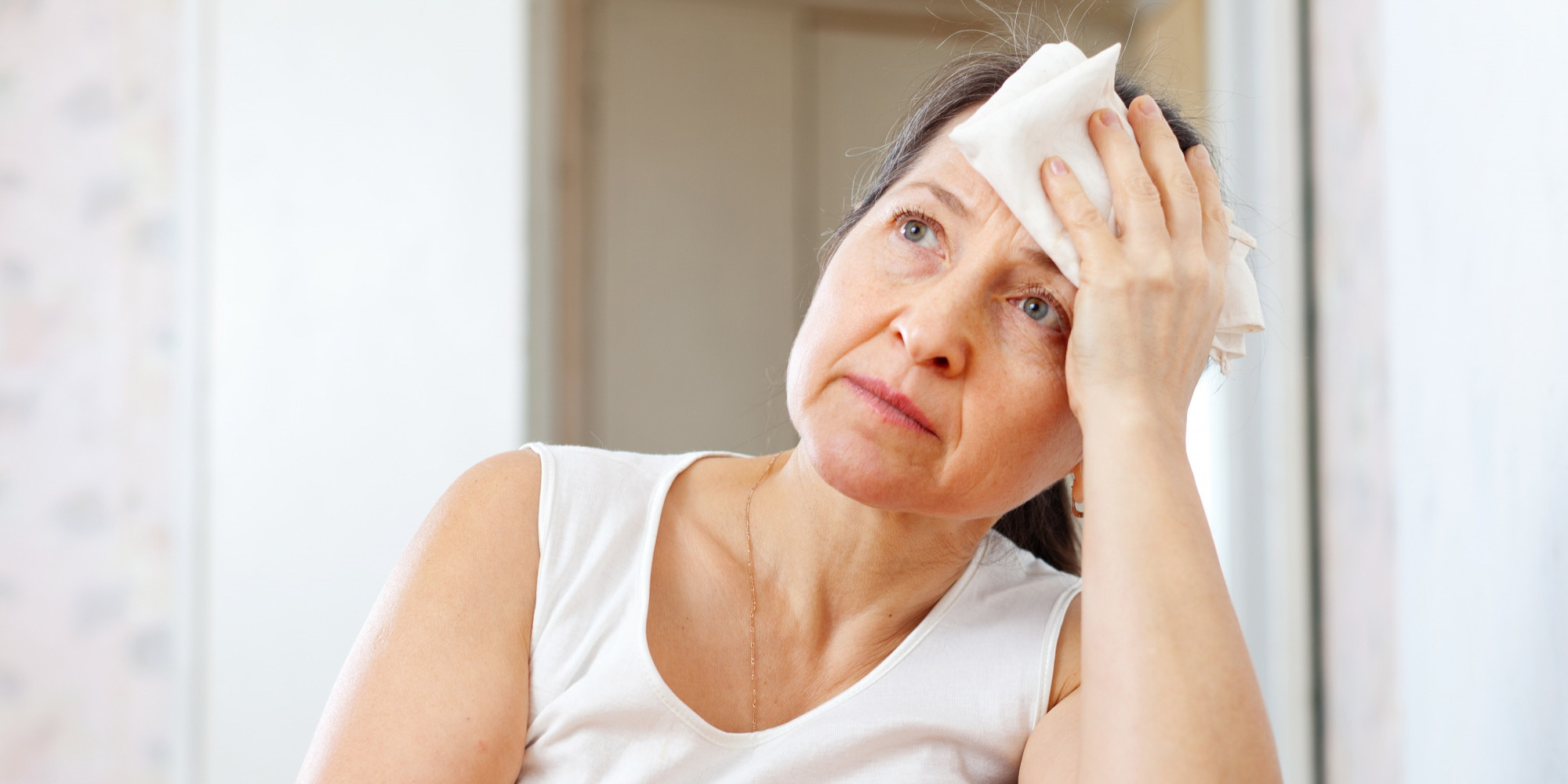 A woman puts a cold towel to her forehead.