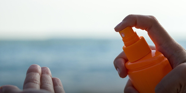 Someone spraying suncream into their hands at the beach