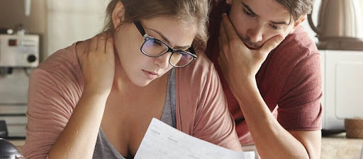 Two adults sit in the kitchen looking at a bill in despair
