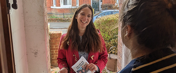 Emma stands on a doorstep talking to a resident