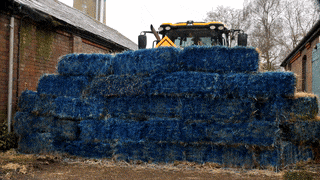 A tractor ploughing through a Blue Wall of hay bales
